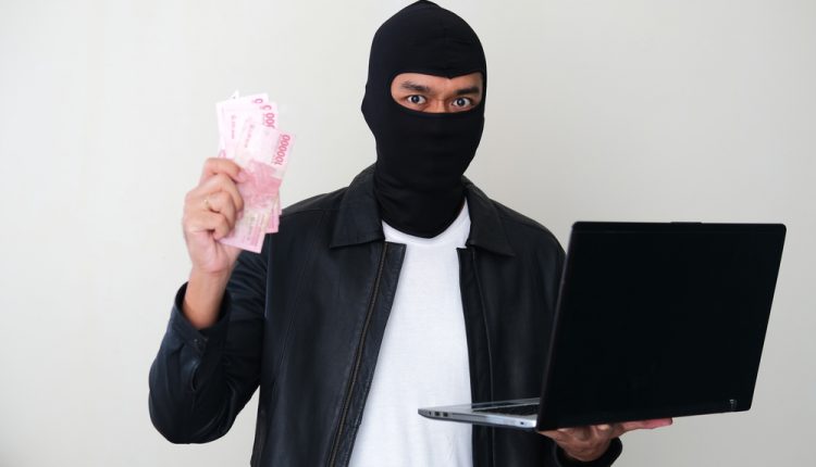 Bad guy wearing balaclava stealing money using a laptop computer